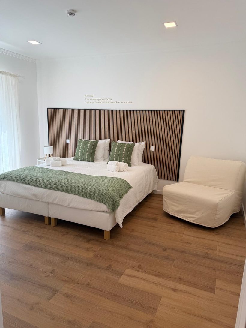 Quarto Respirar com cama de casal, manta verde e painel de madeira ripada