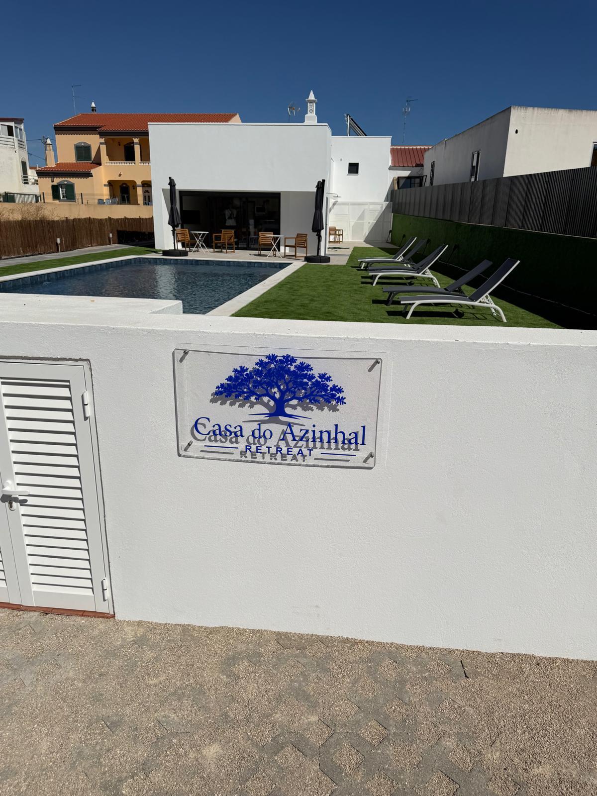 Piscina e jardim da Casa do Azinhal Retreat vistos da entrada, com a placa da casa
